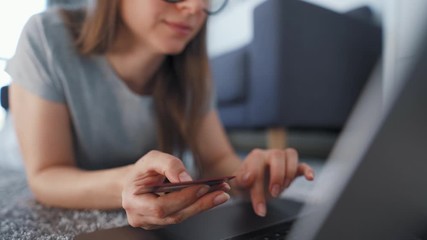 Woman is lying on the floor and and makes an online purchase using a credit card and laptop. Online shopping, lifestyle technology
