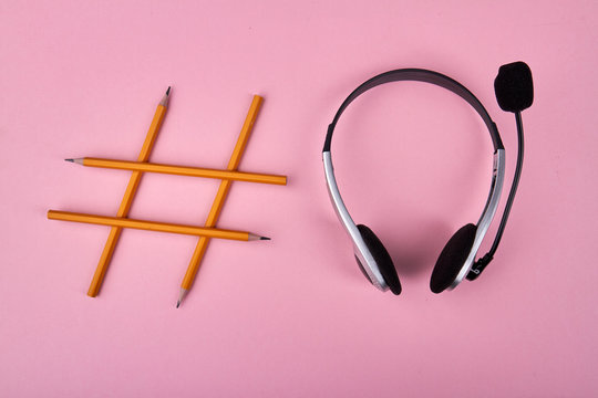 Hashtag symbol made with yellow pencils and headset. Isolated on pink background. Trendy headset concept.