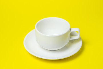 empty cup on a saucer on a yellow background. The cup and saucer are white. A tea set