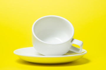 Fototapeta premium empty cup on a saucer on a yellow background. The cup and saucer are white. A tea set