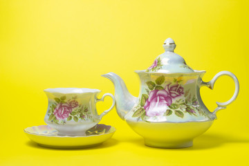 Tea set on a yellow background. A cup and saucer and a teapot next to it. Tea set with flower decorations