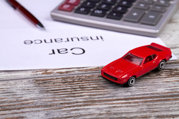 Car insurance accounting concept. Red toy car with calculator and pen on wooden table.