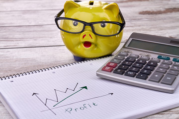Smart investment concept. Piggy bank with calculator and profit growth charts on wooden table.