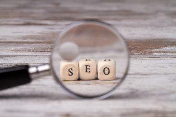 Search engine optimization concept. Looking through a magnifying glass on seo blocks. Seo written on wood block and magnifier isolated on retro wooden background.