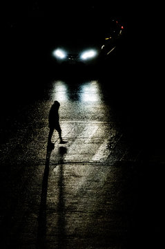 Pedone attraversa la strada illuminata da un'auto