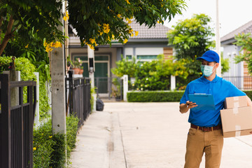 Fototapeta na wymiar Asian young delivery man courier hold parcel post boxes he protective face mask service and walk looking for customer home location, under curfew pandemic coronavirus COVID-19