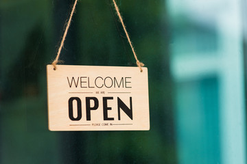 Close up of WELCOME WE ARE OPEN PLEASE COME IN notice sign wood board label hanging through glass...