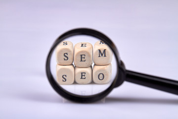 Search engine optimization and marketing concept. Looking through a magnifying glass on wooden blocks with letters. Isolated on white background.