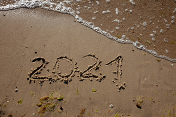 The numbers 2021 are written in the sand. New year on the beach. Sea coast, wave. Natural background. Place for your text. Summer in winter.