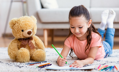 Asian Girl Sketching With Teddy Bear Toy Lying At Home