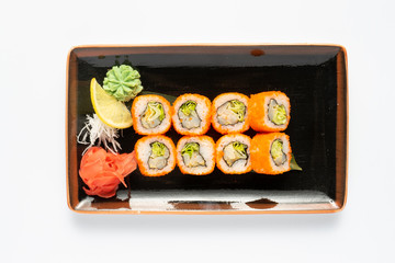 A portion of maki sushi with an assortment of Japanese side dishes in a rectangular ceramic plate on a white plate. Top view.