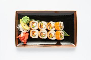 A portion of maki sushi with an assortment of Japanese side dishes in a rectangular ceramic plate on a white plate. Top view.