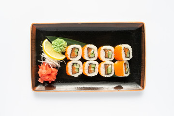 A portion of maki sushi with an assortment of Japanese side dishes in a rectangular ceramic plate on a white plate. Top view.