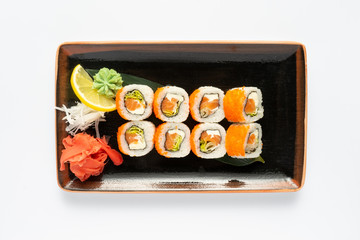 A portion of maki sushi with an assortment of Japanese side dishes in a rectangular ceramic plate on a white plate. Top view.