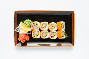 A portion of maki sushi with an assortment of Japanese side dishes in a rectangular ceramic plate on a white plate. Top view.
