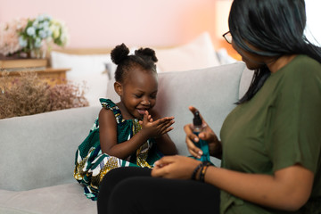 Young African American mother use spray sanitizer on hands child in a protective mask in living...