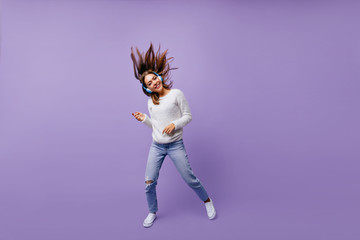 Cheerful, slightly crazy girl playing imaginary guitar, listening to big headphones in big headphones. Studio portrait of musician with dark hair flying