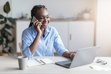 Smiling black female entrepreneur talking on cellphone at workplace in office