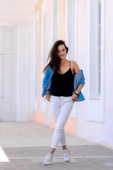 Summer in the city. Fashionable urban girl in casual clothes. Posing in big light hall. Long brown hair. Hands in pockets.