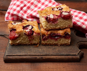 stack of square baked sponge cake slices with plums on wooden kitchen board