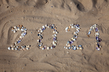 The numbers 2021 are written and lined with seashells in the sand. New year on the beach. Sea coast. Place for your text. Summer in winter. Natural background.