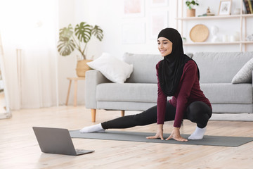 Sporty muslim woman in hijab exercising at home, watching tutorials on laptop