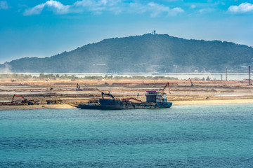 Self-propelled sand carrier barges, lorry, backhoe and other land moving machinery perform ground...