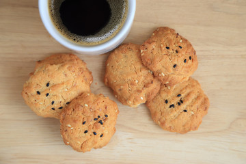 Tasty sesame cookies, one bitten piece and black coffee.