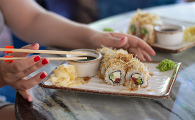 Woman eating sushi set with soy sauce, wasabi and sticks in restaurant