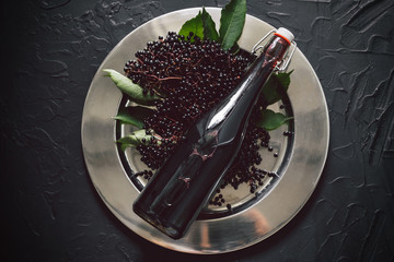 A bottle of elderberry syrup on a dark background with fresh elderberries 