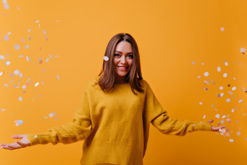 Happy adorable woman in yellow sweater laughing on bright background. Indoor portrait of appealing girl posing with confetti.