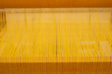 Close up of yellow silk on a weaving machine and Thai silk. A loom for producing homemade silk in Thailand.
