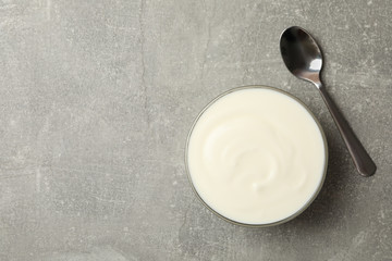 Spoon and bowl of sour cream on gray background, top view