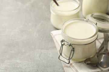 Glass jars of yogurt, spoons and napkin on gray background
