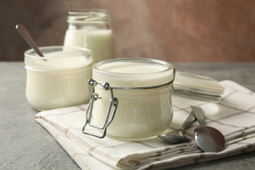 Glass jars of yogurt, spoons and napkin on gray background