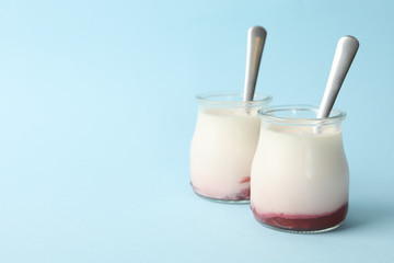 Glass jars of yogurt with spoons on blue background