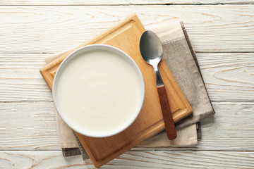 Sour cream yogurt, spoons and napkin on white wooden background