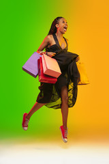 Jumping high, flying with shopping bags. Portrait of young woman in neon light on gradient...