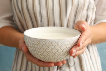 Woman in apron hold bowl of sour cream yogurt against blue background