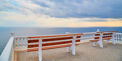 Obraz premium Virgin nature. Summer view. Ocean scenery. Viewing platform with bench. Empty promenade. Stormy dark sky. Calming sea
