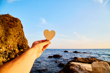 Travel world. Romantic travel. Vacation time. Summer holidays. Male hand holding small heart. Sea, rocks on background