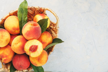 Ripe peaches in a wicker basket on a stone gray table with a juicy peach slice with a stone pit.
