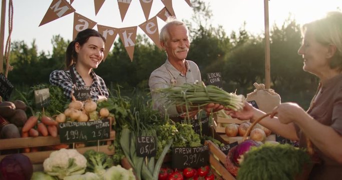 Senior woman buying groceries at local farmers market. Senior man and his daughter offering fresh fruits and vegetables right from the ranch 4k footage