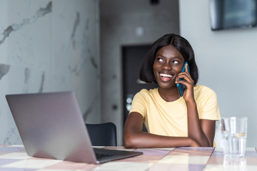 Smiling african woman using mobile phone while sitting on a kitchen at home