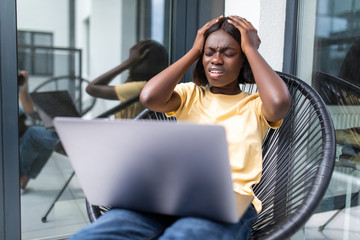 Upset sad beautiful african girl looking at laptop holding cup sitting in chair at balony © F8  \ Suport Ukraine