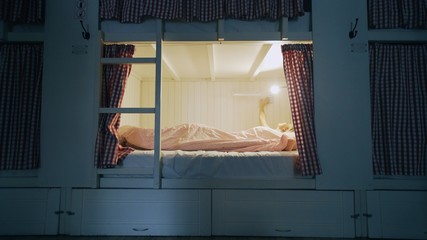 Young girl lays in bed and turns off the light in cozy hostel room