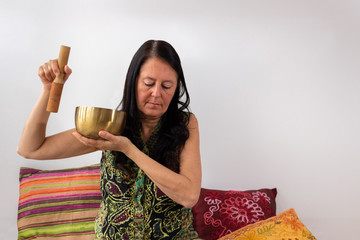 Middle age woman using Tibetan singing bowl with her eyes closed. Concept of relax and zen aura.