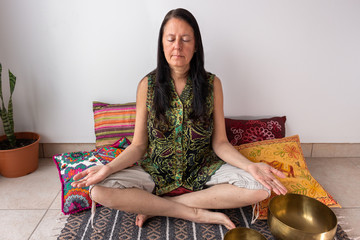 Woman in meditation position with Tibetan singing bowls at her feets. Concept of zen aura y relax.