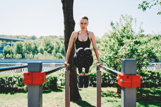 Young sportswoman exercising on parallel bars in park