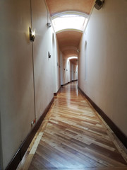 Long corridor with wooden floor with entrance of light and lights on the walls